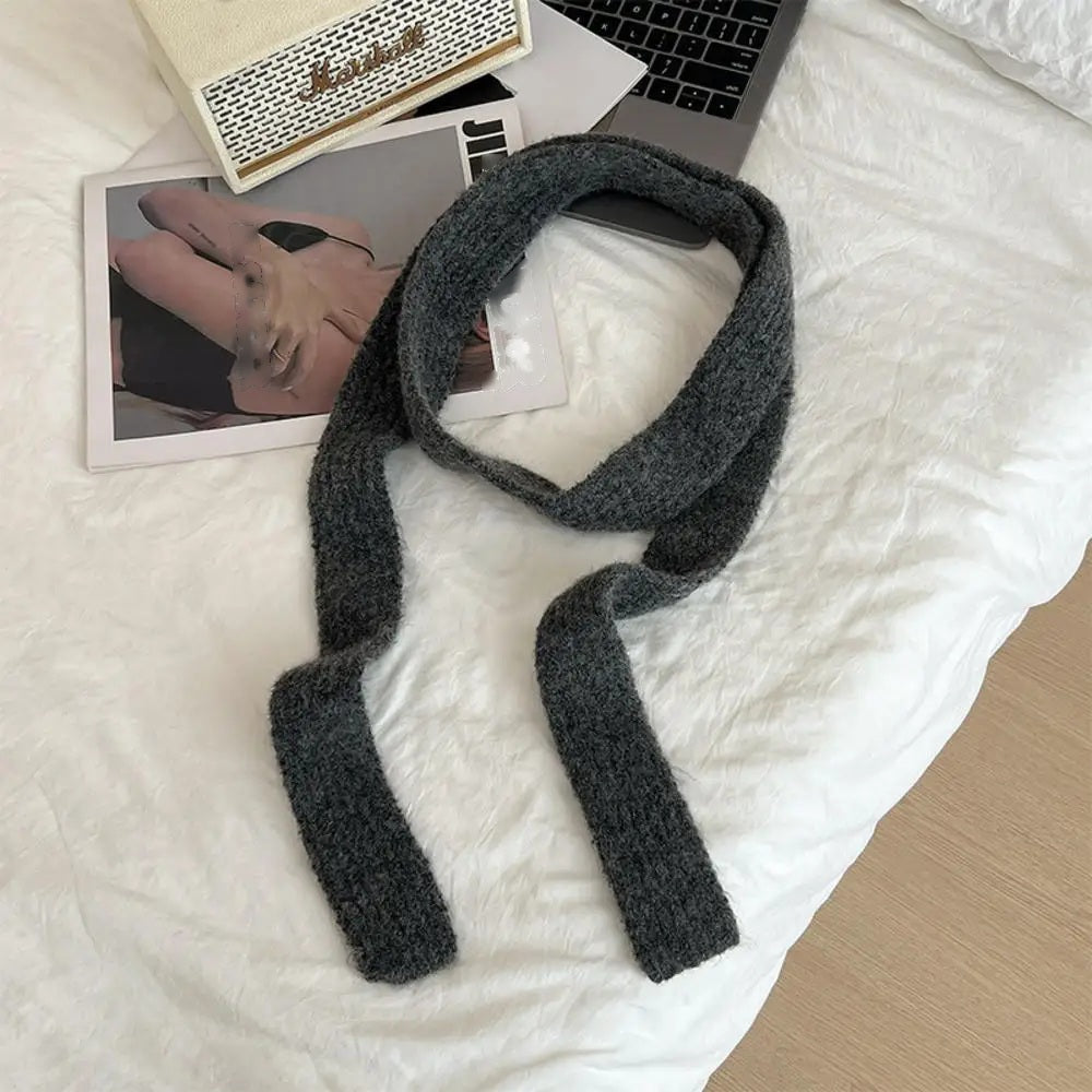 Dark grey cashmere scarf looped, flat lay on white bedding