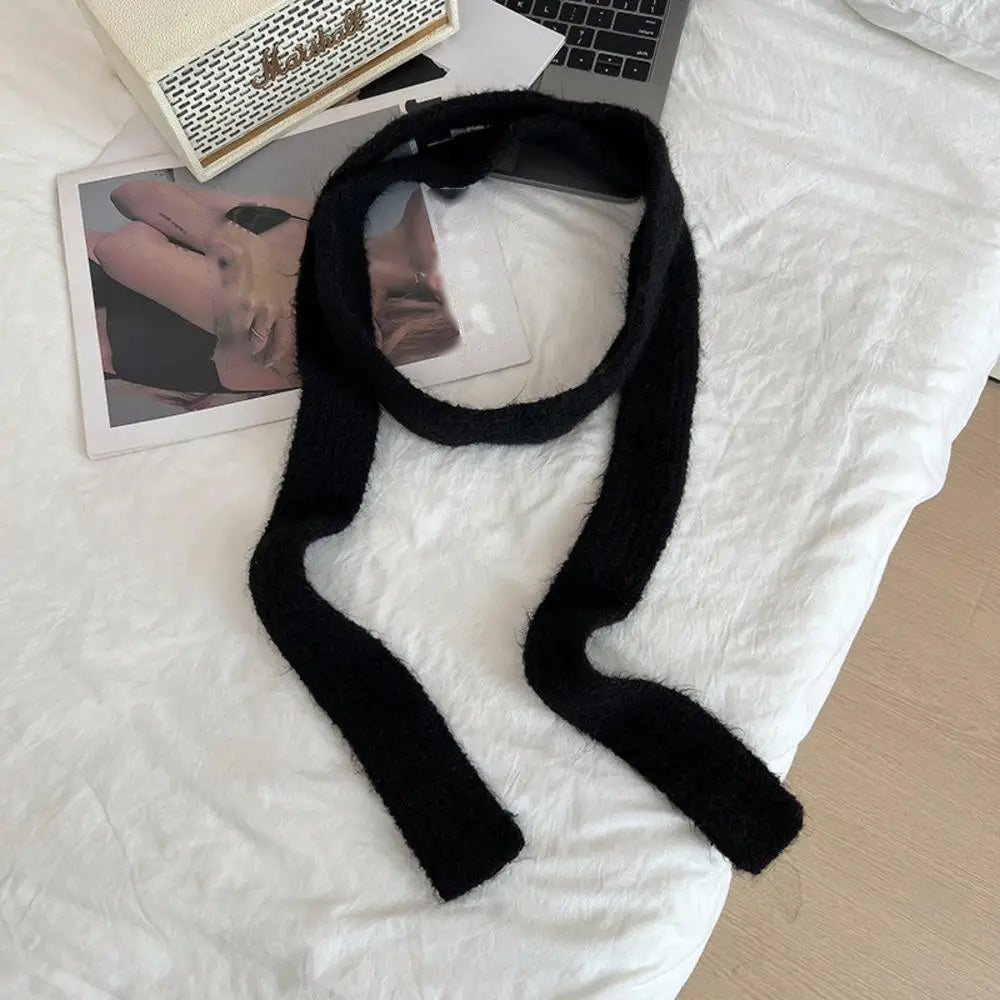Black cashmere scarf looped, flat lay on white bedding