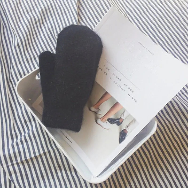 Black knitted mitten resting on an open magazine in a white tray