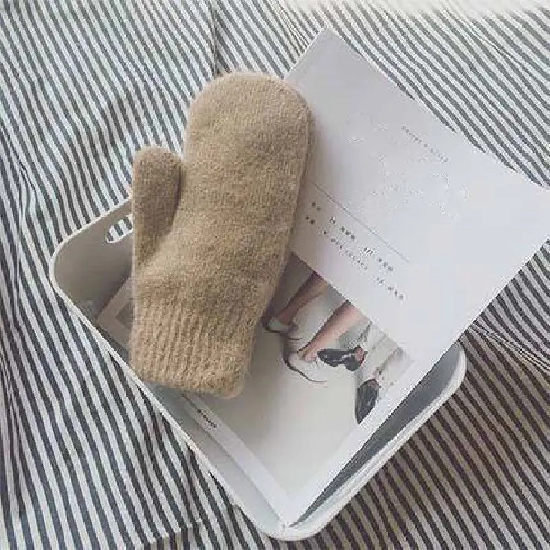 Camel knitted mitten resting on an open magazine in a white tray