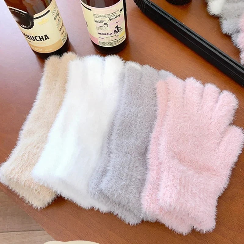 Plush velvet winter gloves in white, grey and pink laid on a wooden table