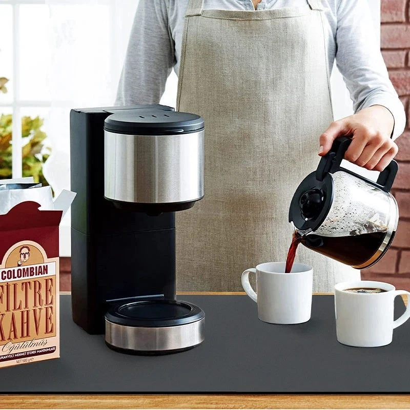 Stainless steel drip coffee maker on a dark kitchen counter beside a coffee pack