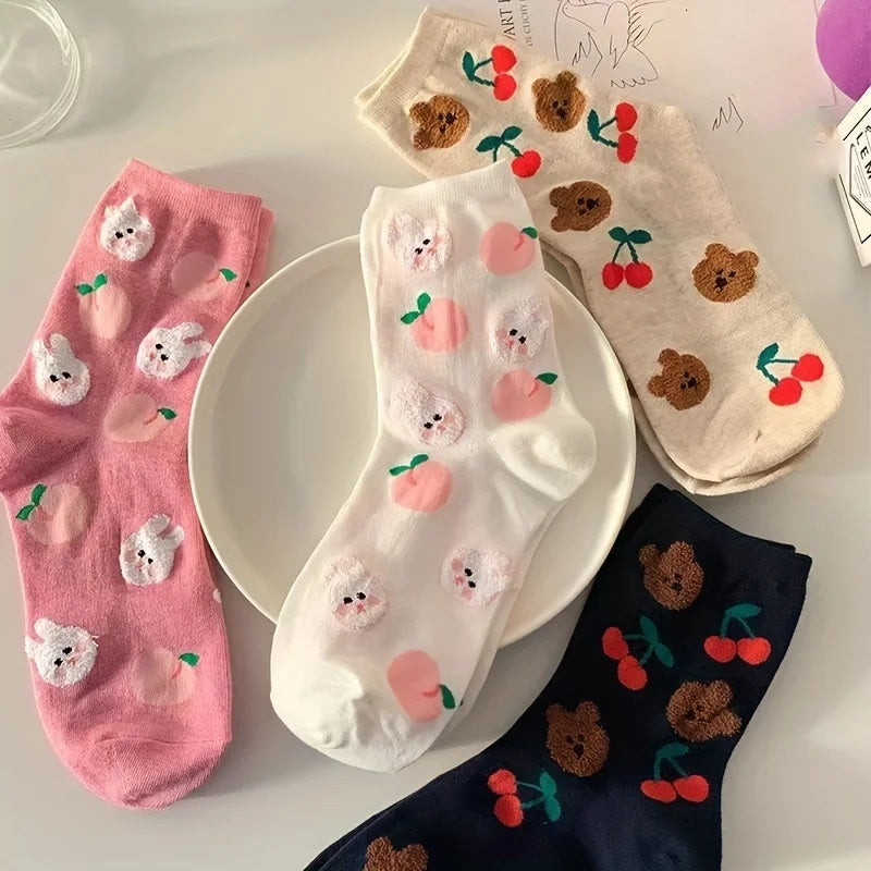 Four pairs of girls' knee high socks with bear, cherry and peach patterns laid out on a pale pink surface