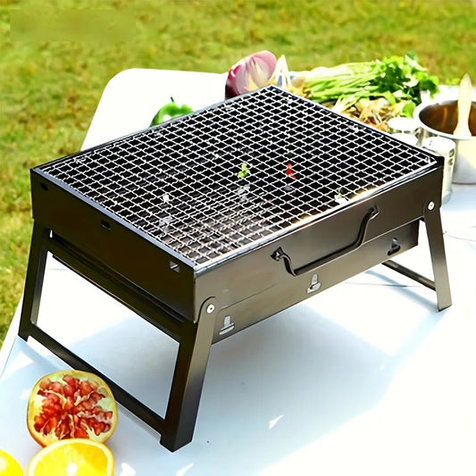Portable stainless steel charcoal barbecue grill set up on a table outdoors with vegetables behind it