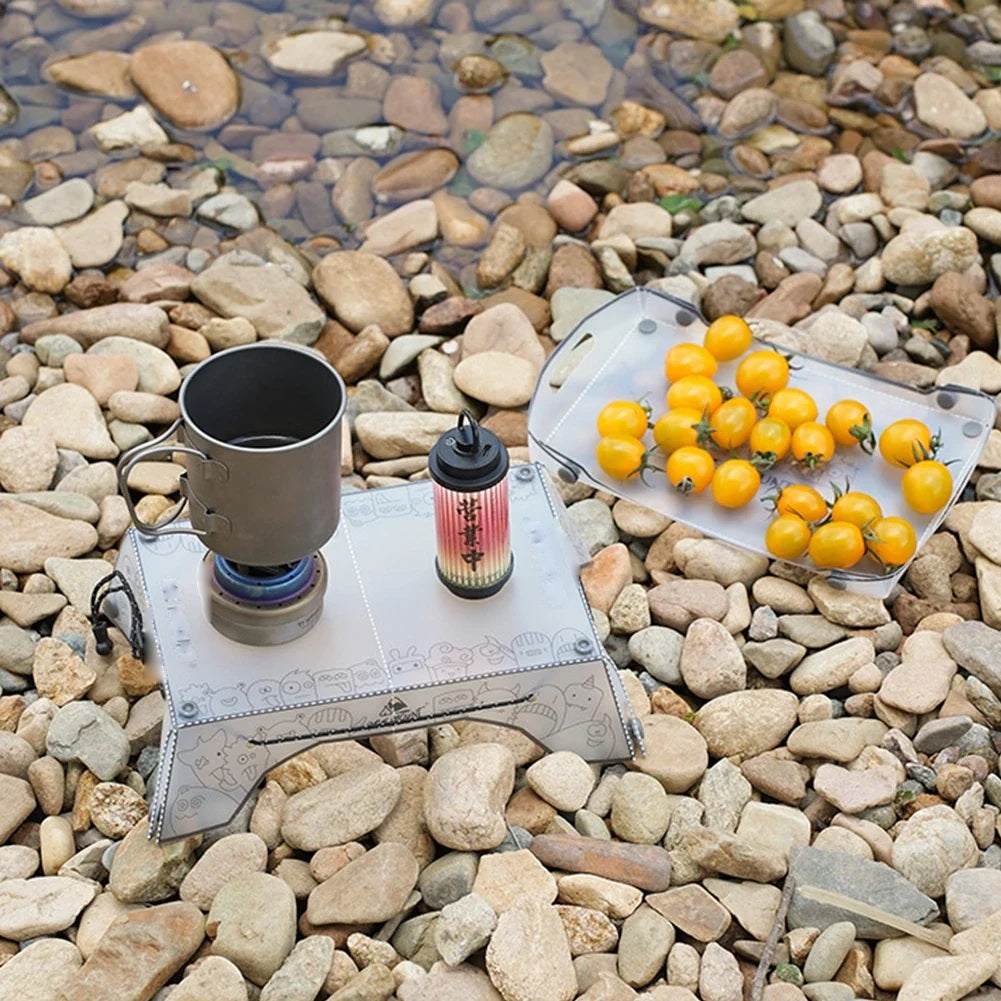 Folding camping table on river stones holding a stove and lantern