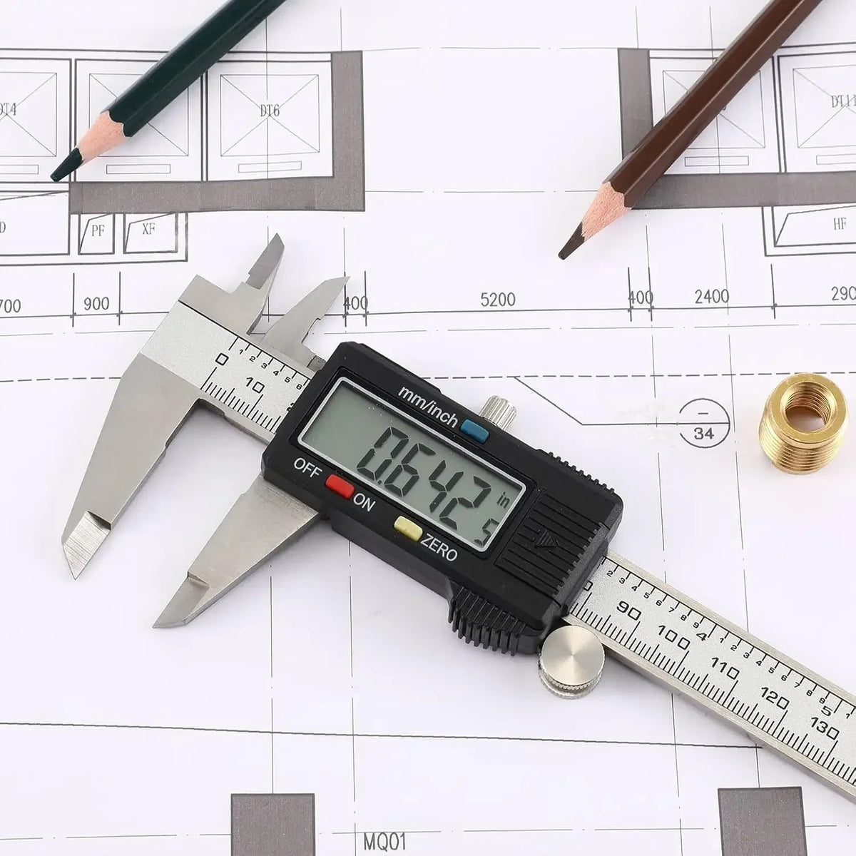 Digital caliper measuring a brass fitting on a technical drawing with pencils