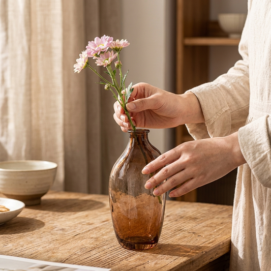 Placing flowers into a brown retro glass vase on a desk